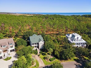 A large, two-story house with a green roof, surrounded by dense forest and a clear view of the ocean. - 5BR/6BA Coastal Retreat with Elevator, Screened Porches & Easy Beach Access (Georgetown)