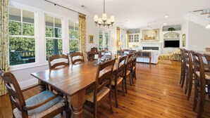 Un'ampia sala da pranzo con un grande tavolo in legno e sedie, un lampadario e ampie finestre con tende.