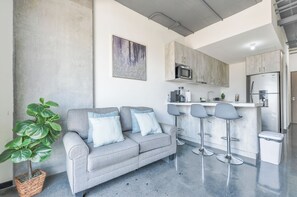 A modern kitchen with a grey countertop, stainless steel appliances, and a bar area with stools. - KYO Constella (Monterrey)