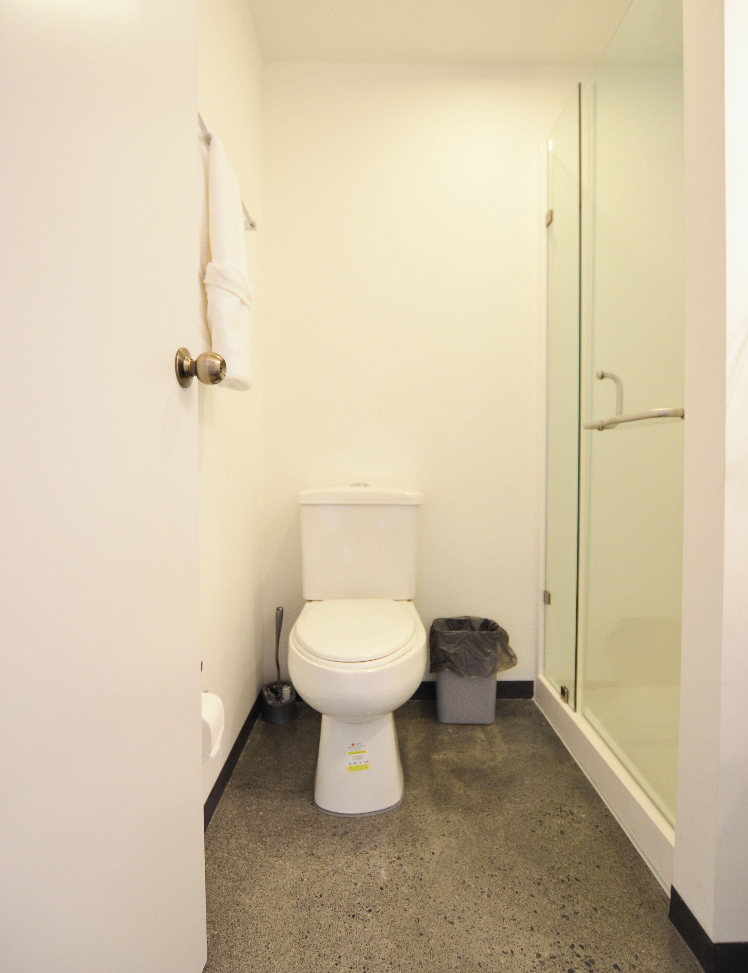 A small, clean bathroom with a toilet, a trash bin, and a glass shower door.