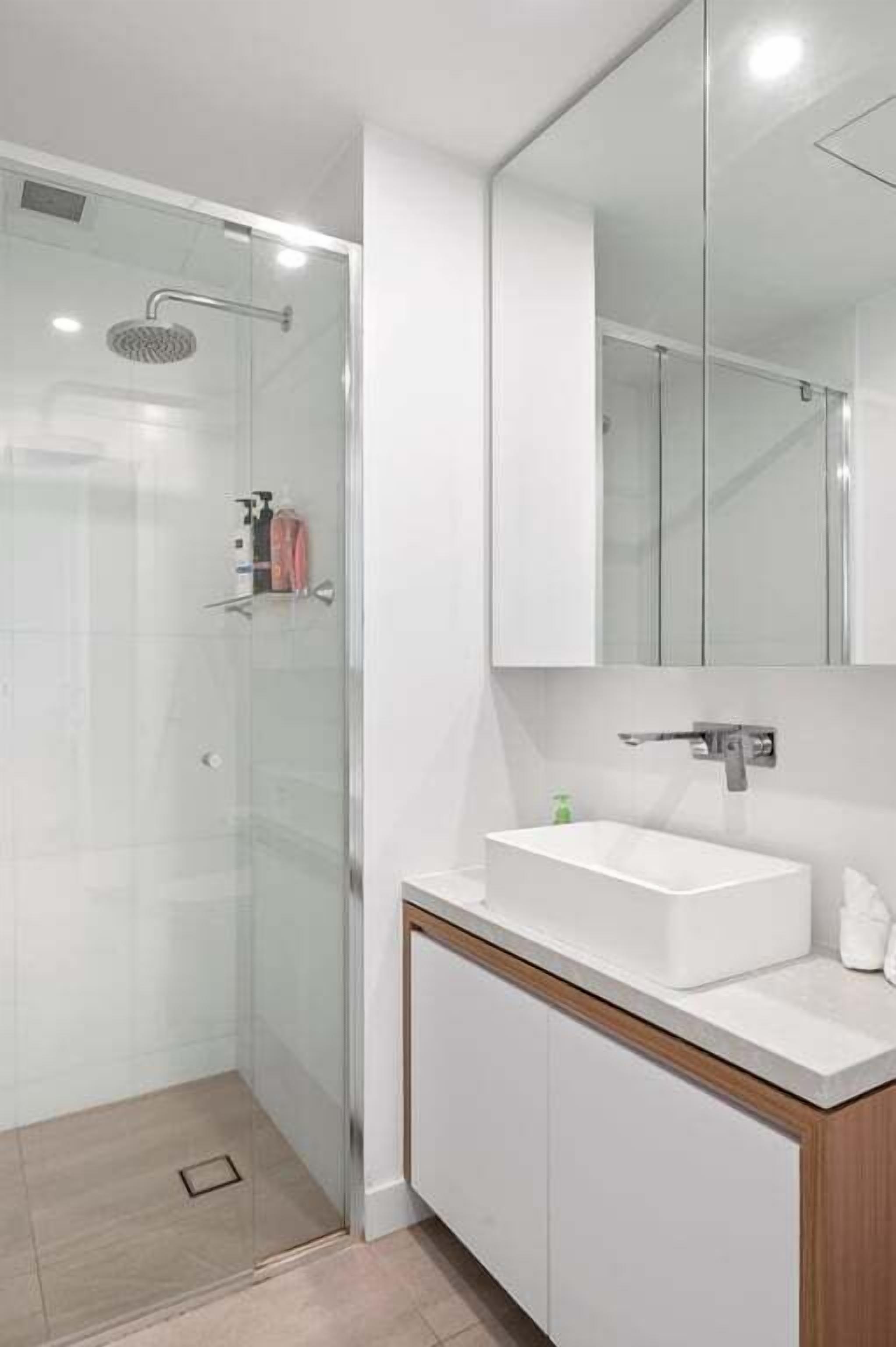 Un baño moderno con ducha de vidrio, un lavabo blanco y un espejo grande sobre el tocador.