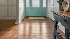 Ein Korridor mit Holzdielen, einer türkisblauen Tür, weißen Wänden und einem Kronleuchter.