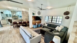 A spacious living area with a grey sofa, a dark grey couch, and a dining table with chairs. There is a kitchen in the background with white cabinets and a patterned backsplash. - Fabulous 4-bedroom Home, 900 Meters from Ocean in Cozumel (San Miguel de Cozumel)