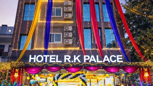 A multi-story hotel with balconies, air conditioning units, and a well-lit entrance with colorful drapes and string lights. - Hotel RK palace near airport (Jaipur)