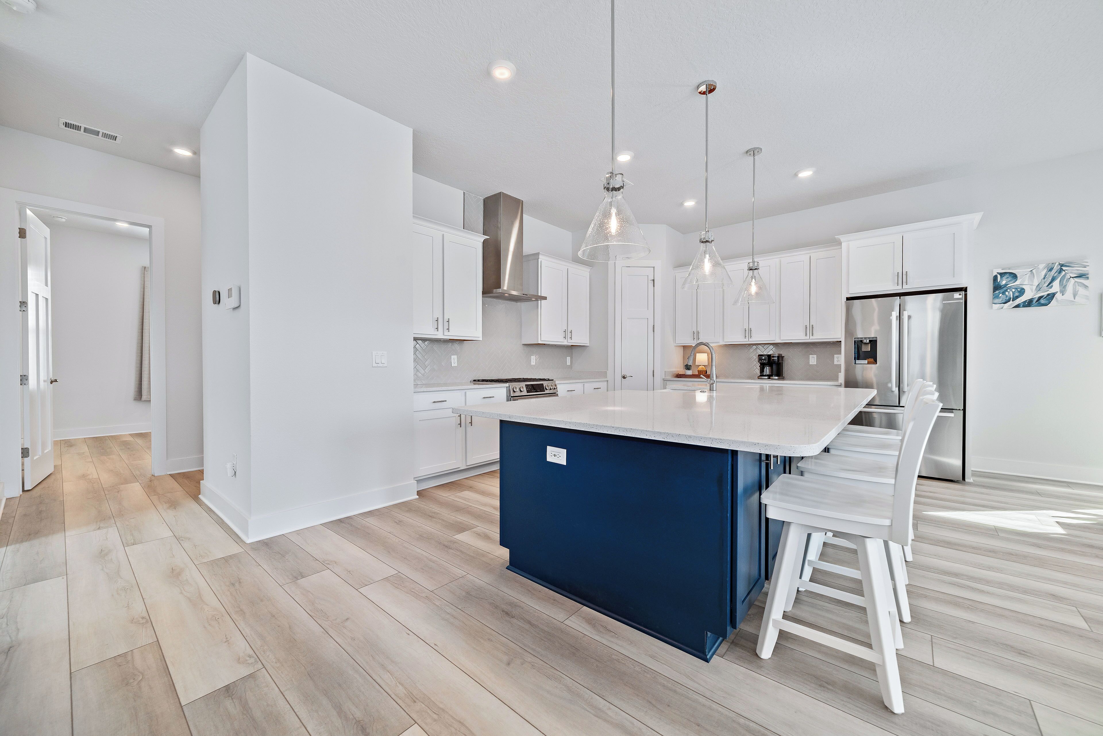 A modern kitchen with white cabinets, a blue island, stainless steel appliances, and pendant lighting.