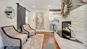 A living room with two patterned armchairs, a fireplace, and a wall-mounted mirror. - Island Square condo #808 (Saint Simons Island)