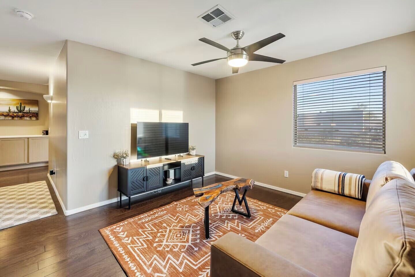 A modern living room with a flat-screen TV, a ceiling fan, a sofa, and a patterned rug.