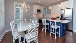 Una cocina moderna con armarios blancos, una isla central y un comedor con sillas blancas.