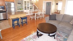 Une cuisine moderne avec un îlot central, un coin repas avec des chaises blanches, un canapé et une table basse.