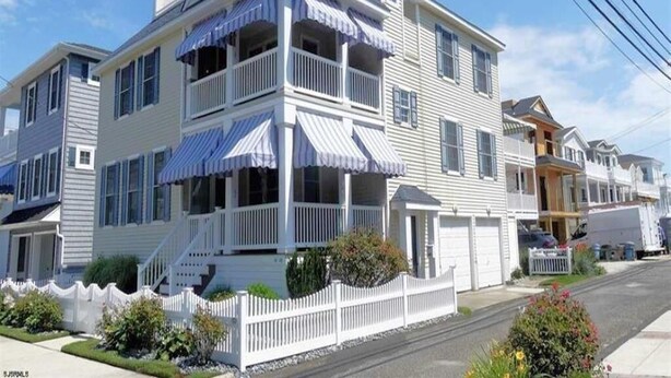 Une maison à deux étages avec un balcon, une clôture blanche en bois et un ciel bleu dégagé.