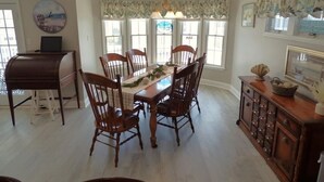 A dining room with a wooden table and chairs, a chandelier, and a window with a view of the beach. - Comfortable Southend 4BR Condo • Sleeps 8 • Deck, Parking & Outdoor Shower (Ocean City)