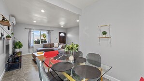A modern living room with a glass dining table, a sofa, and a coffee table. There are plants on shelves and a hanging plant. - Tranquil 2-bedroom house with AC in pleasant Rosemead (Rosemead)