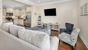 A modern living room with a sofa, a chair, a flat-screen TV, and a kitchen in the background. - Close to Island Amenities (St. Simons Island)