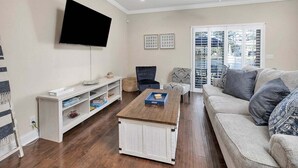 A living room with a flat-screen TV, a wooden coffee table, a sofa, and a chair. - Close to Island Amenities (St. Simons Island)