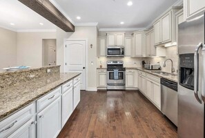 A modern kitchen with white cabinets, granite countertops, stainless steel appliances, and a wooden floor. - Close to Island Amenities (St. Simons Island)