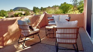 Un patio con sedie e cuscini in vimini, vista su una collina e un edificio sullo sfondo.