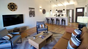 Un soggiorno moderno con televisione a schermo piatto, un divano, un tavolino da caffè e un angolo cottura con frigorifero, microonde e sgabelli da bar.