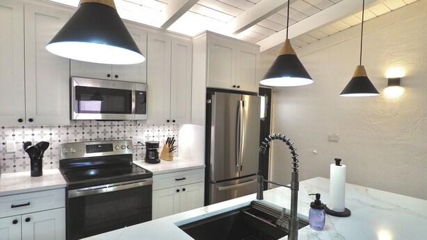 Cucina moderna con mobili bianchi, frigorifero in acciaio inossidabile, microonde, lavello con rubinetteria moderna e illuminazione a sospensione.
