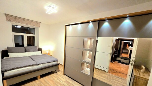 A bedroom with a bed, bedside table, and a wardrobe with a mirror. - Executive apartment + terrace + private parking space (Chemnitz)