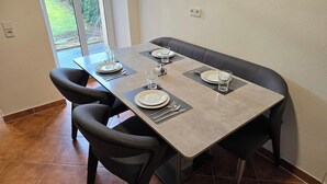 A dining area with a rectangular table set for four, two chairs on each side, and a view of a garden through a glass door. - Executive apartment + terrace + private parking space (Chemnitz)