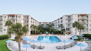 Ein Hotel mit einem zentral gelegenen Schwimmbad, umgeben von Liegestühlen und Sonnenschirmen, mit mehreren Etagen und Balkonen.