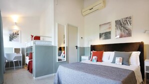 A compact hotel room with a bunk bed, a desk, and a bed with multiple pillows. - Villa Elprado (Cervia)