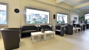 A modern lounge area with leather sofas, a white coffee table, and large windows offering a view of greenery. - Villa Elprado (Cervia)