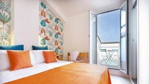 A hotel room with a large bed, a desk, a chair, and a balcony with a glass door. - Villa Elprado (Cervia)