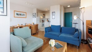 A living room with a blue sofa, a light green sofa, and a dining area with a wooden table and chairs. - Appartement Paloma, vue océan - Welkeys (Soorts-Hossegor)