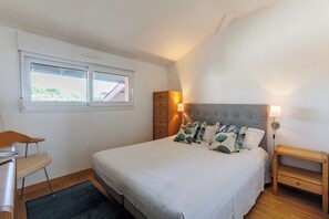 Ein Schlafzimmer mit Bett, Nachttischen, einem Sessel, einem Schreibtisch, einem Fenster und einem Kleiderschrank.