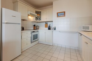 Eine Küche mit weißen Schränken, einem Liebherr-Kühlschrank, einem Backofen, einer Mikrowelle und einem Geschirrspüler.