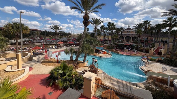 Een resort met een groot zwembad, palmbomen en uitzicht op de omliggende gebouwen.