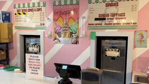 Een ijssalon met een roze-wit gestreepte muur, een menubord en een ijsmachine.