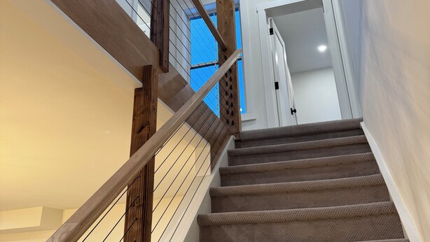 Una scala con ringhiere in legno e gradini rivestiti di tappeto conduce a una stanza con una porta bianca e una finestra con tende blu.