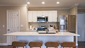 A modern kitchen with white cabinets, stainless steel appliances, and a bar area with four stools. - Big Water Views, Private Dock, 7 Kayaks, Sleeps 12 (Sparta)