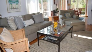 Una sala de estar con un sofá, sillones, una mesa de centro de vidrio y un comedor con mesa y sillas.