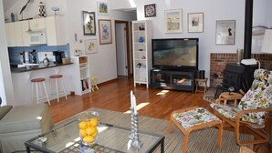 Una sala de estar con televisor, chimenea y una zona de cocina con taburetes.