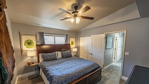 Ein Schlafzimmer mit Bett, Deckenventilator, Fenster und Tür zu einem weiteren Raum.