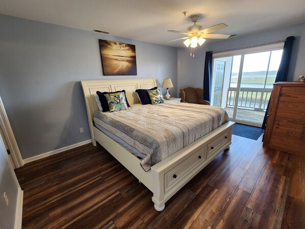Une chambre à coucher avec un lit, un ventilateur de plafond, une vue sur l’extérieur et un plancher en bois.