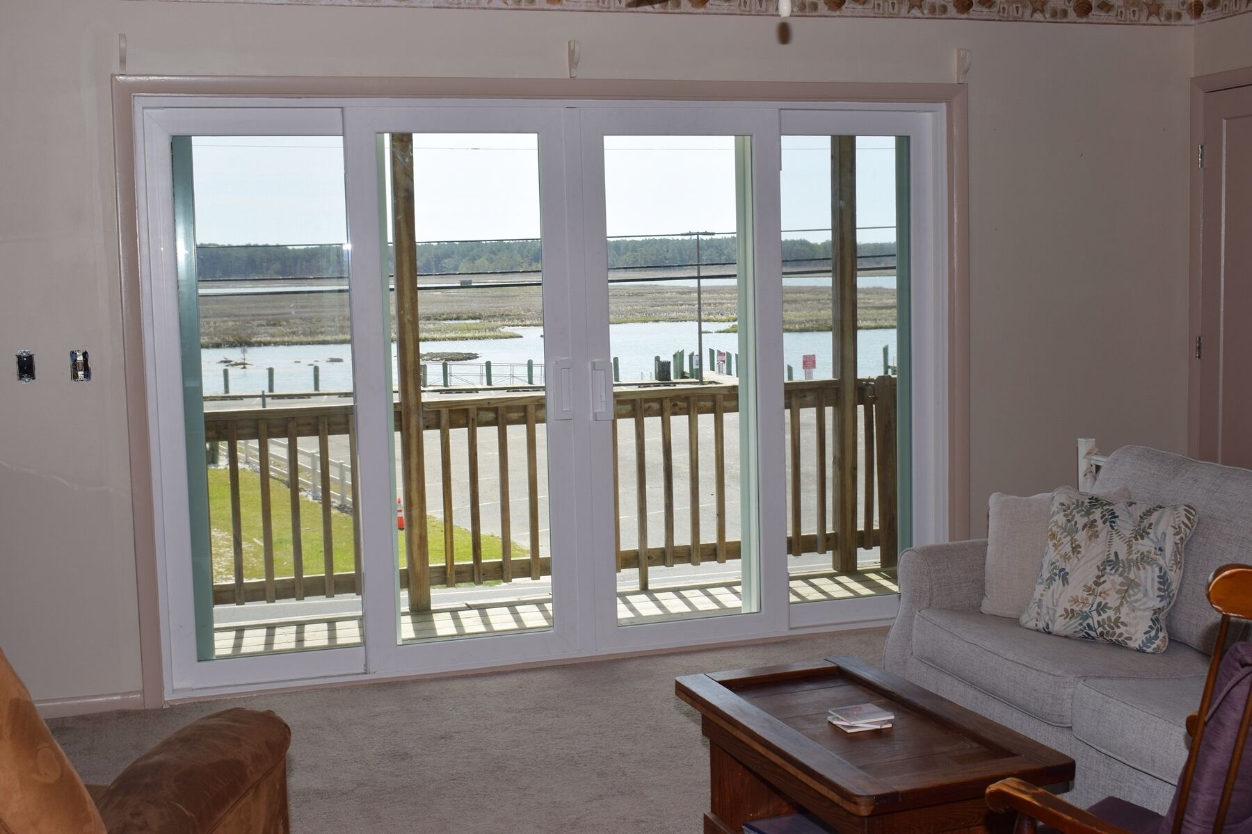 Ein Zimmer mit einer Schiebetür und einem Balkon mit Blick auf ein Gewässer und eine Holzterrasse.