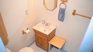 Ein Badezimmer mit Toilette, Waschbecken, Holzschrank und einem kleinen Hocker.