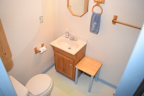 A bathroom with a toilet, sink, wooden cabinet, and a small wooden stool. - Paradise by the Lighthouse | Waterfront Chincoteague Retreat (Chincoteague Island)