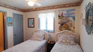 Ein Schlafzimmer mit zwei Einzelbetten, einem Deckenventilator, einem Fenster mit Blick auf einen Leuchtturm und maritimer Dekoration.