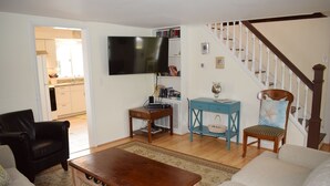 Un salon comprenant un canapé, une table basse, un téléviseur, une bibliothèque et un escalier.