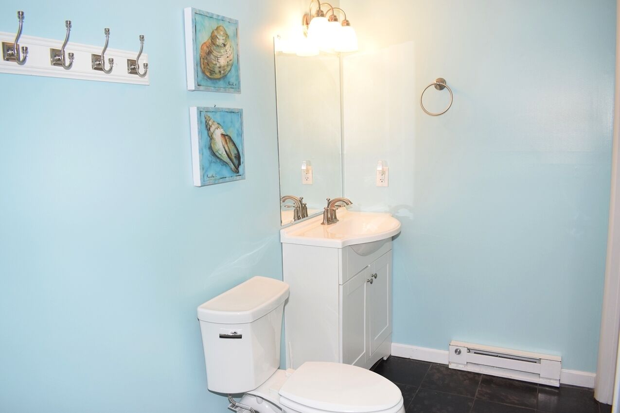 A bathroom with a toilet, sink, and mirror. There are two wall-mounted hooks and two framed pictures.
