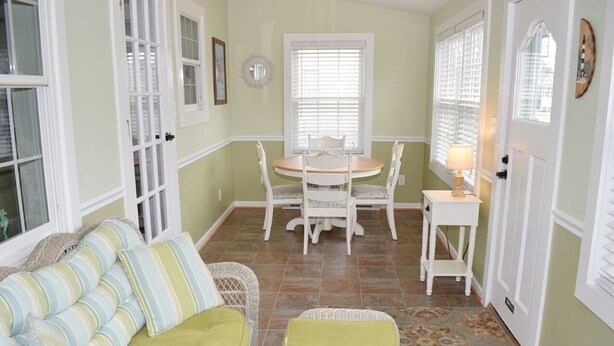 Une pièce chaleureuse avec un canapé vert, une petite table ronde entourée de chaises et une porte dotée d’une fenêtre.