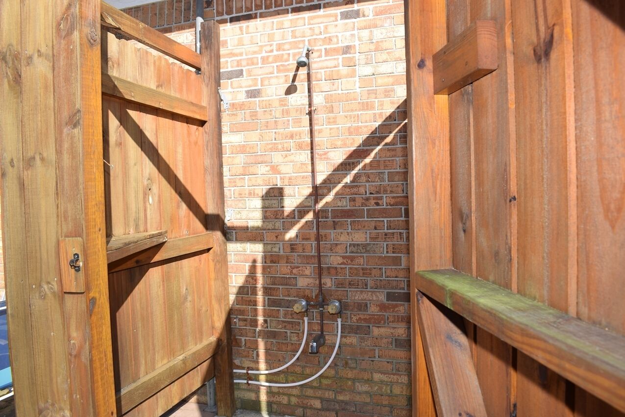 A wooden outdoor shower with a brick wall background.