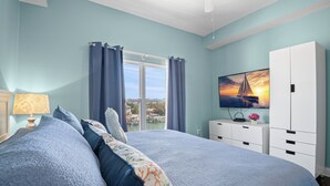 Ein Schlafzimmer mit einem großen Bett, einem Fernseher, einem Fenster mit Vorhängen und Blick auf ein Gewässer.