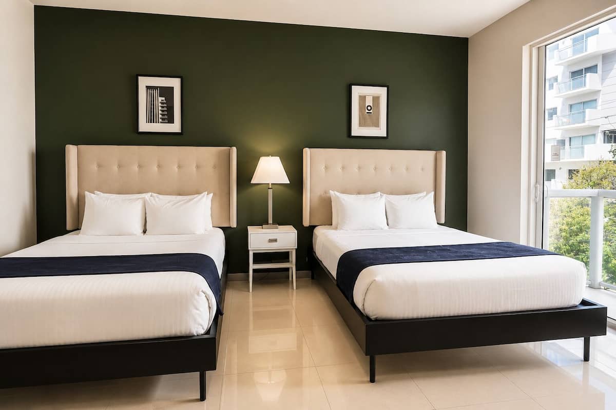 A hotel room with two beds, a nightstand with a lamp, and artwork on the walls.