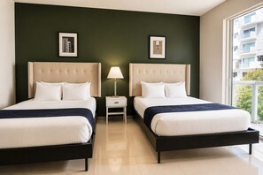 Habitación de hotel con dos camas, una mesita de noche con lámpara y cuadros en las paredes.